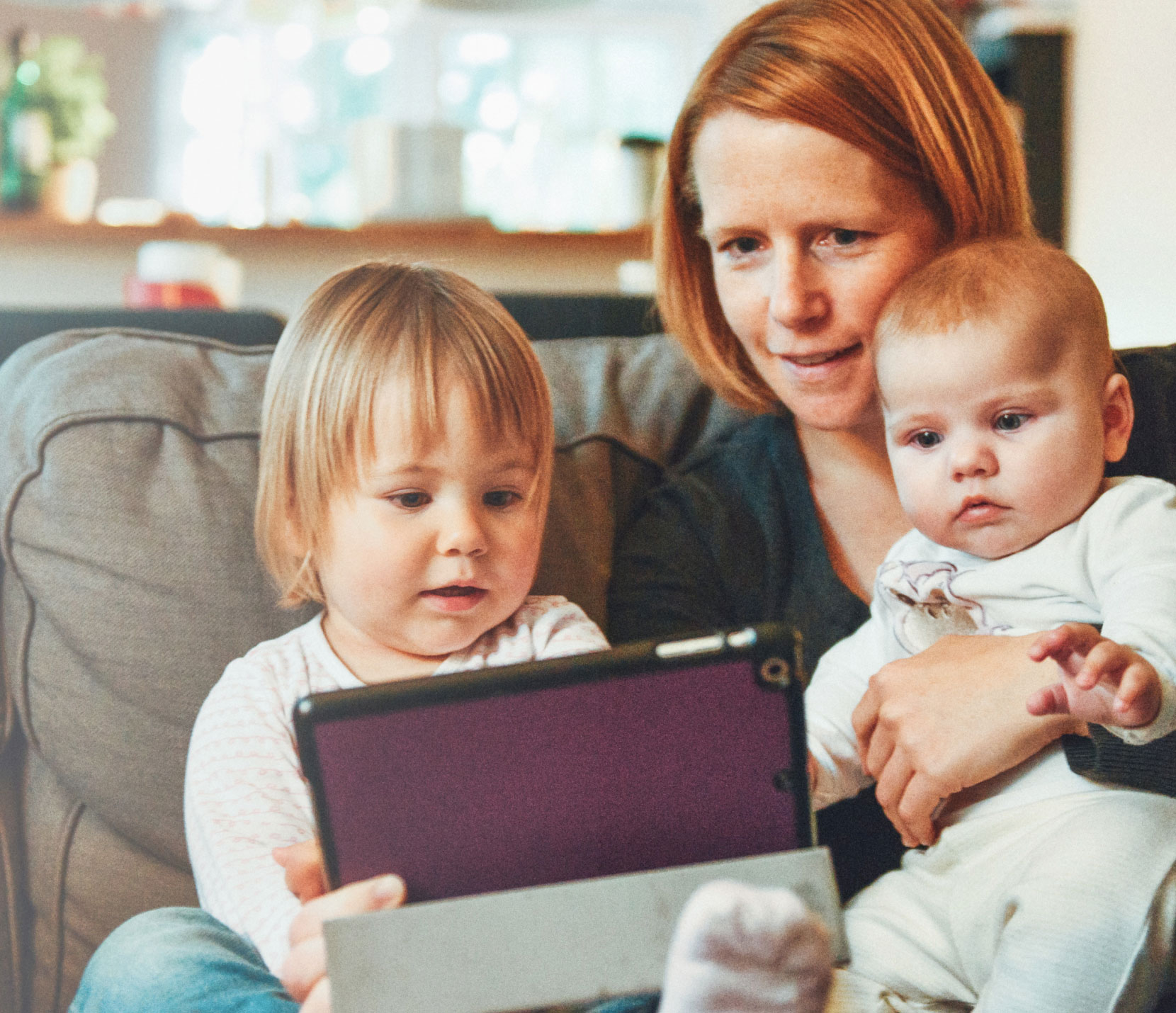 mom with young kids sitting on a couch looking at a tablet