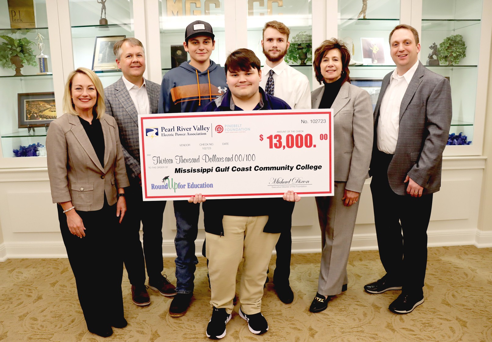 young man surrounded by a group of people holding a 13 thousand dollar check for a program called round up for education. 