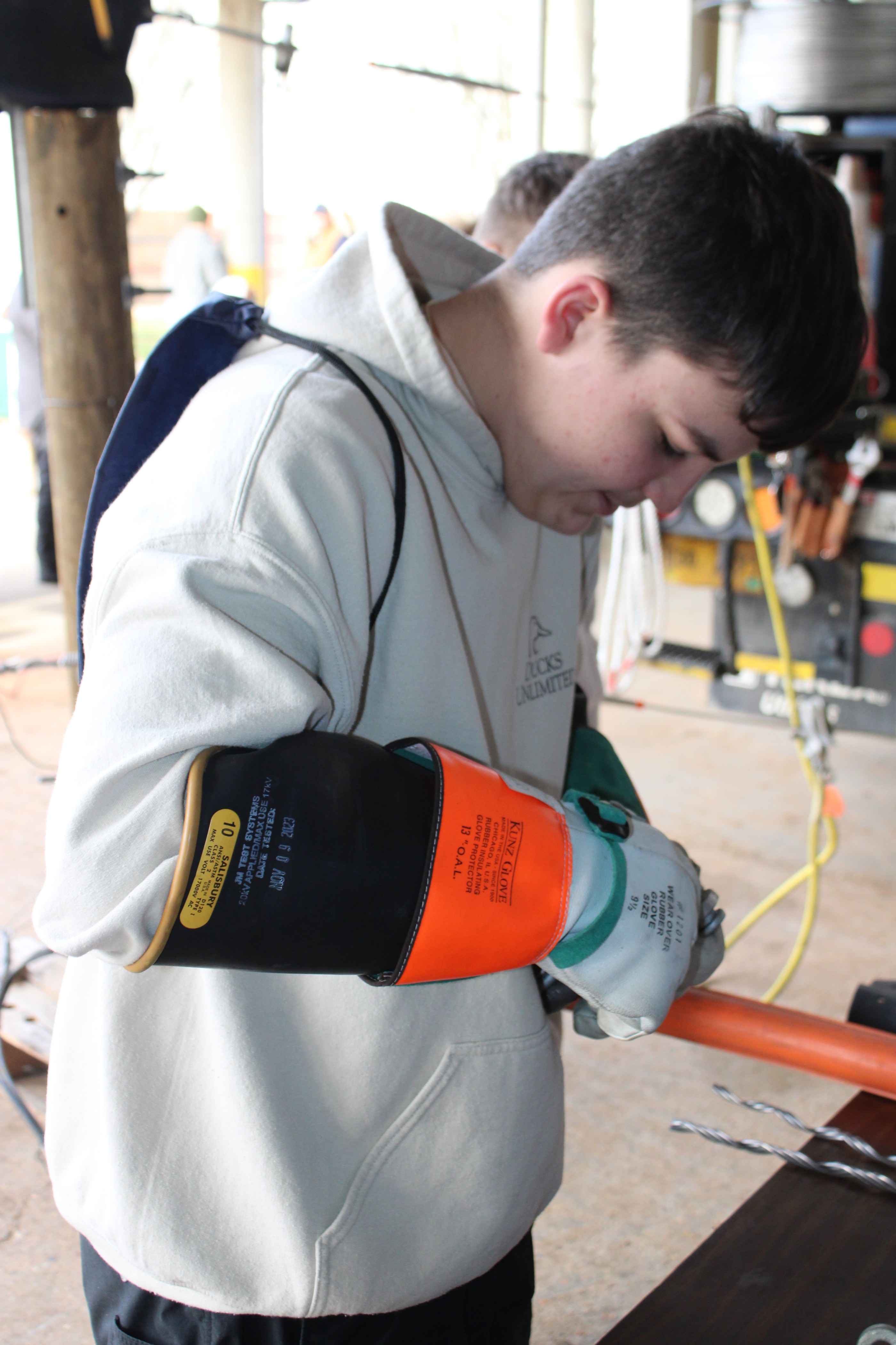 Grade school boy using electrical tools and gloves in a safe workshop place while following instructor instructions